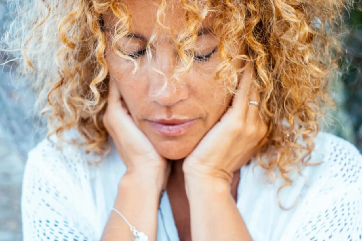 Introspection concept with mature woman touching softly her face with both hands having thoughts and difficulty concept life moments.